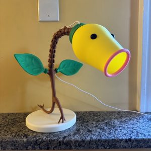 3D Printed "BellSprout" Pokemon lamp with green leaves, brown stem, and yellow head on countertop.